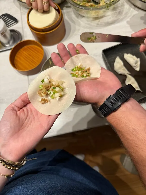 Two hands holding an uncooked gyoza, a circular piece of dough filled with some ingredients.