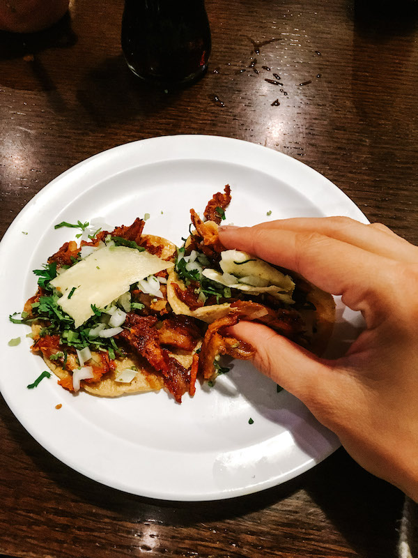 A hand holding a taco on top of a plate with another taco during a food tour in Mexico City.