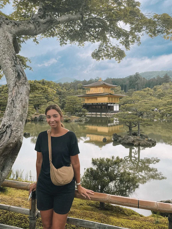 Woman standing in front of Kinkaku-ji temple in Kyoto, also known as Golden Pavillion because of its color.