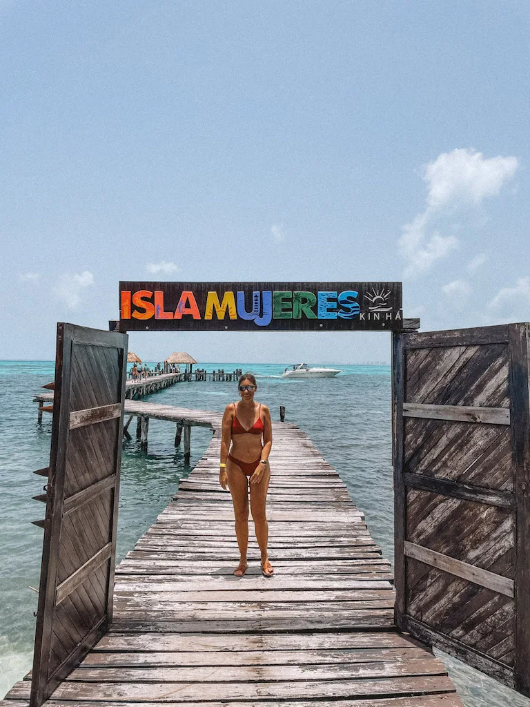 A girl with a red swimsuit standing on a wooden pier over the ocean under a sign that says 