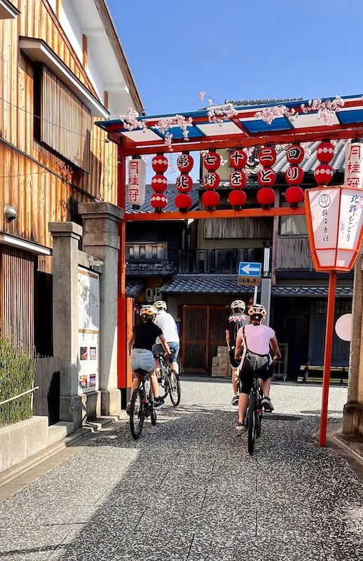 Four people on their bikes wearing helmets passing under a red gate.