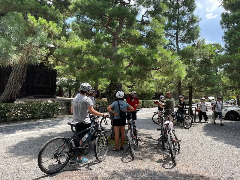 A group of people wearing helmets and holding their bikes while listening to theri guide.