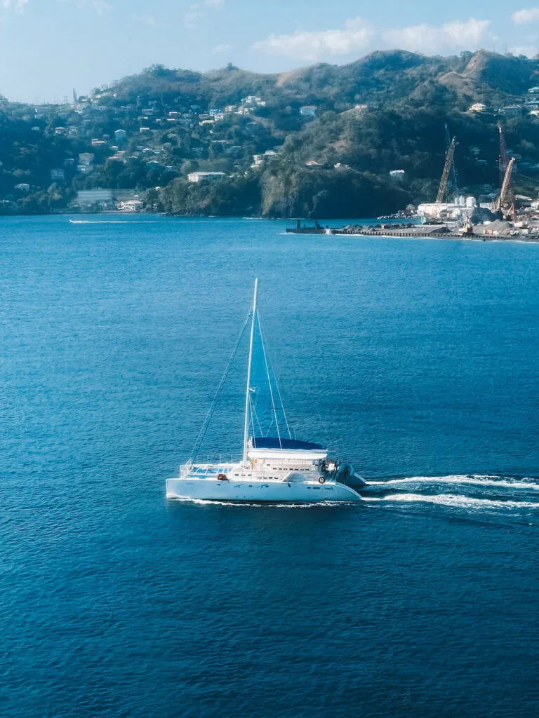 A yacht sailing on blue waters, with a clifftop town in the distance