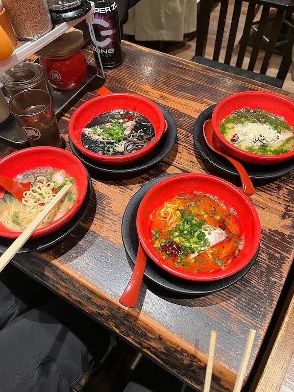 Four red bowls of ramen with different toppings.