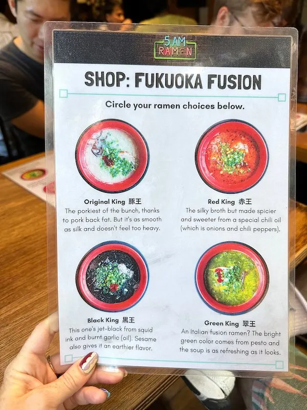 A hand holding a menu with multiple types of ramen.