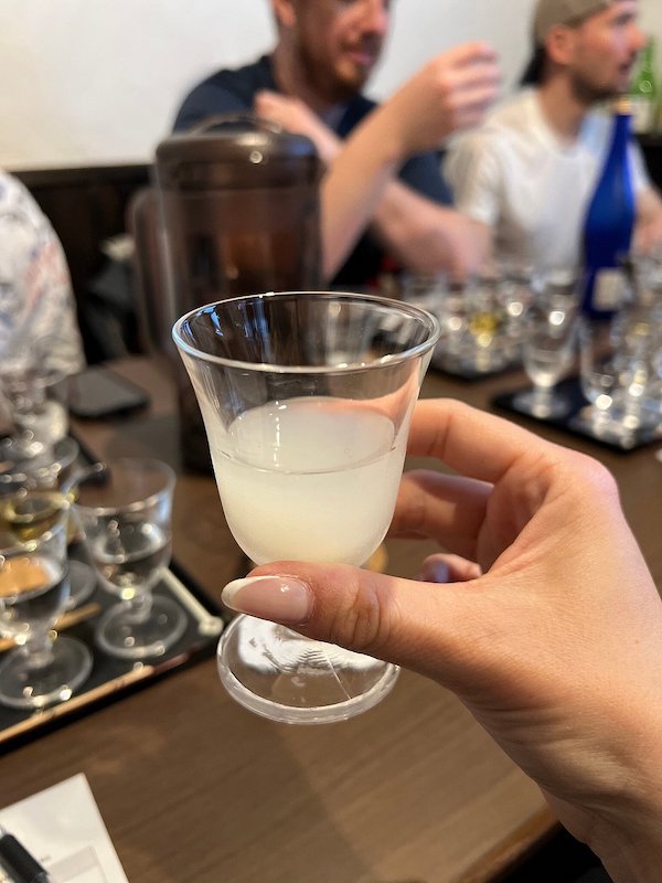 A woman's hand holding a tiny glass with a hazy white liquid inside.