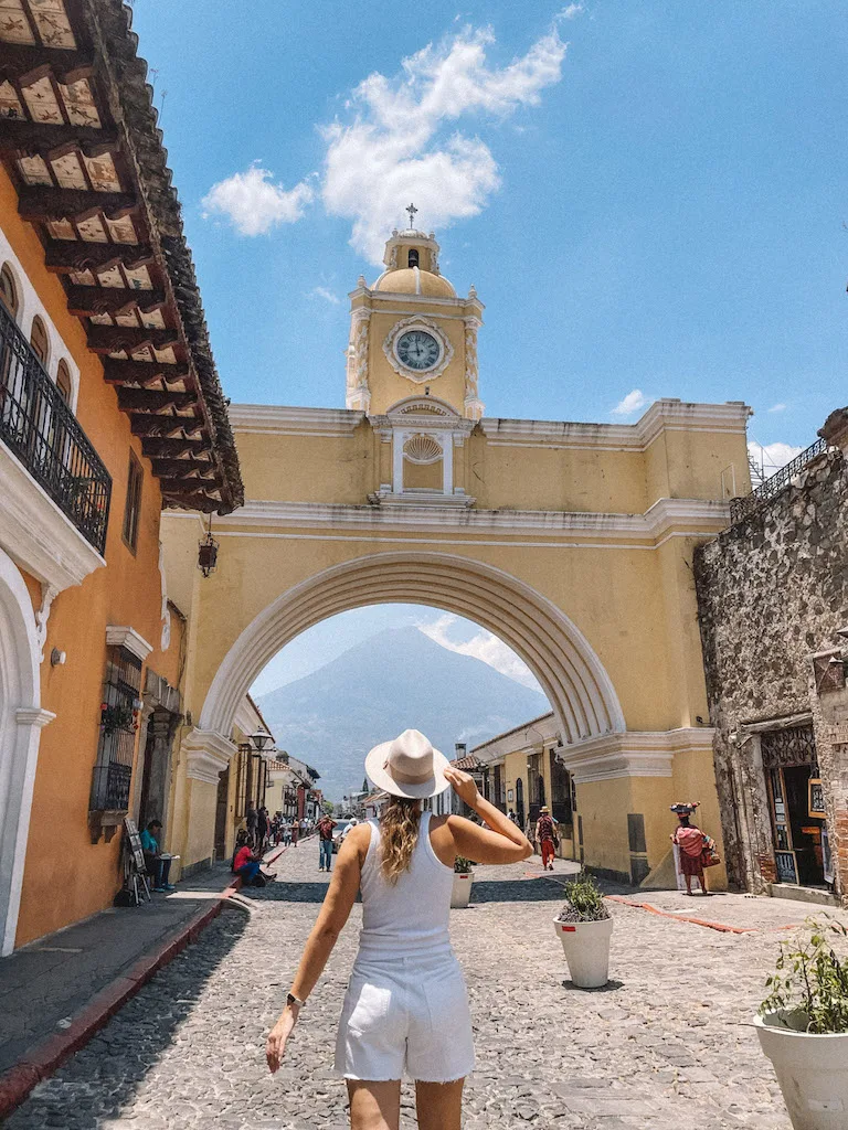 A woman standing in front of the yellow arch in Antigua, with a volcano in the background 