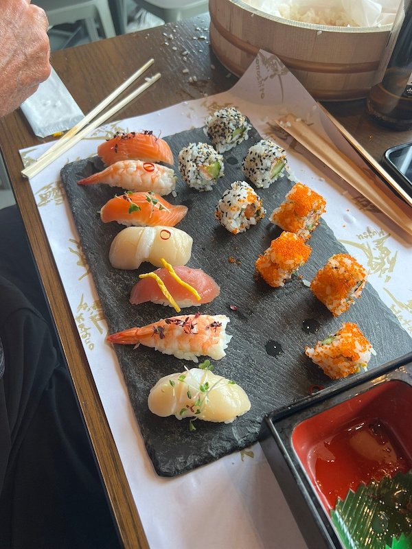 A tray full of pieces of sushi and nigiri and two chopsticks.