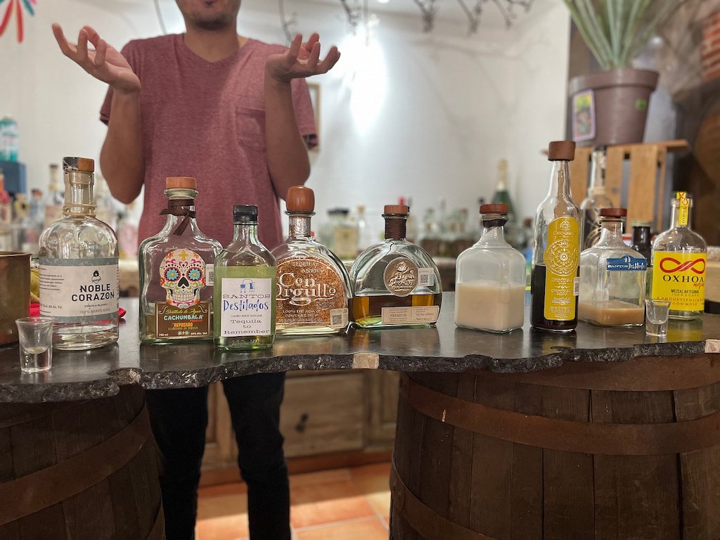 Man standing behind a table covered by bottles of tequila and mezcal.