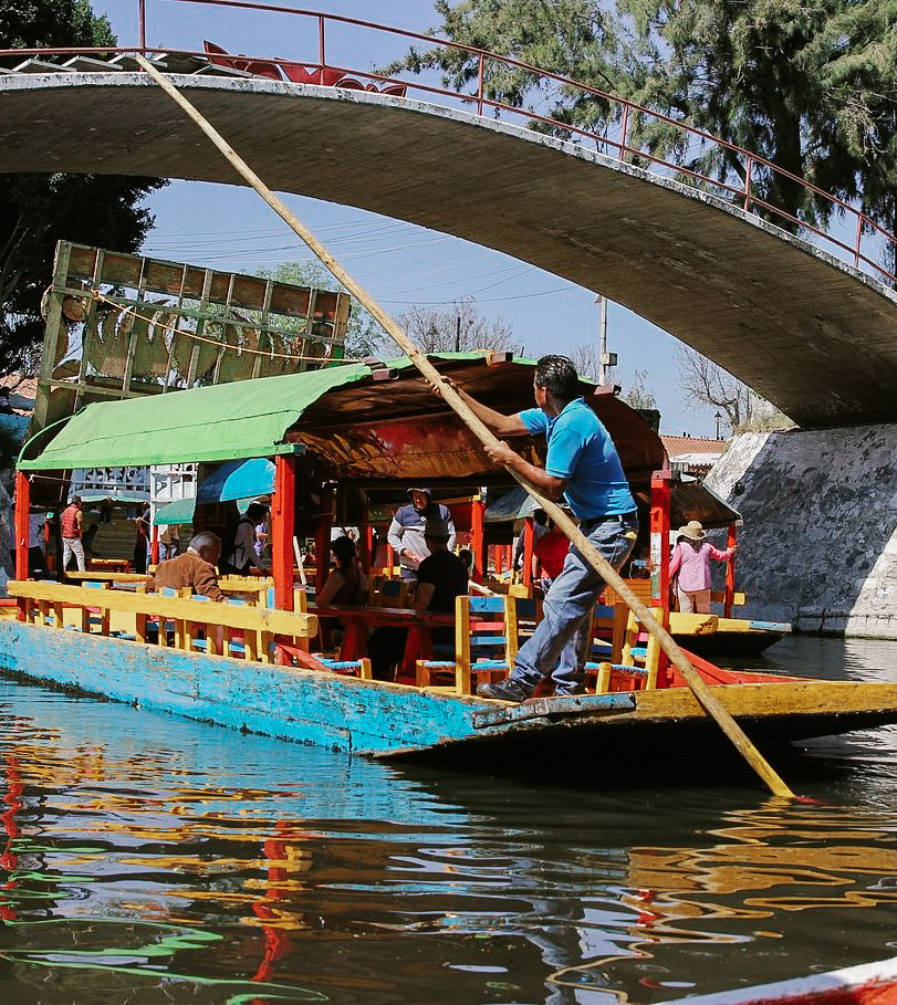 Man driving a colorful boat in a canal in Xochimilco.