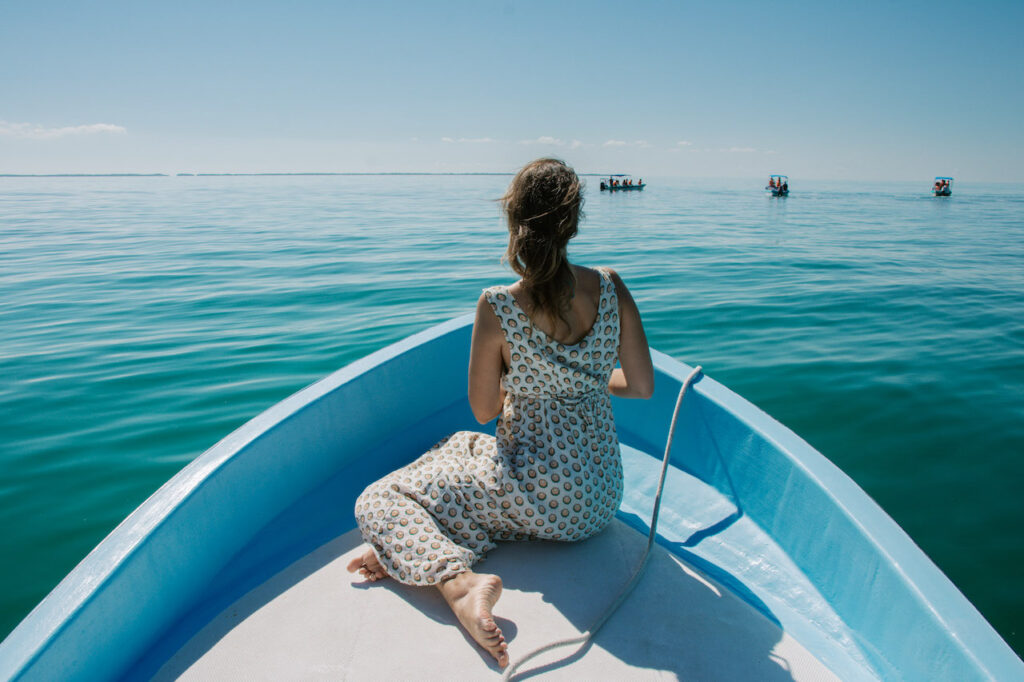 Woman sitting at the end of a small blue boat in the middle of the sea.