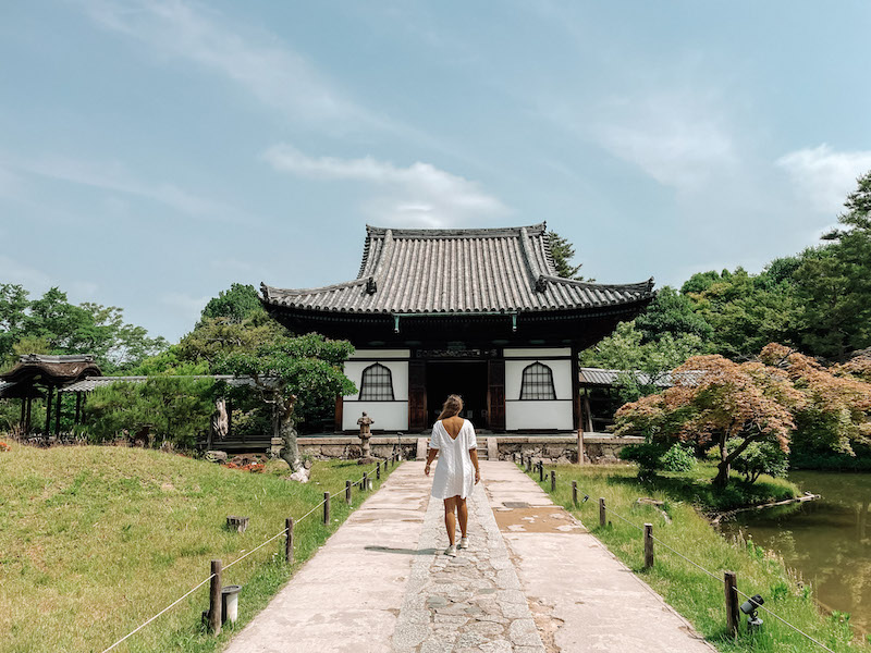 A woman with a white dress standing in front of a shrine surrounded by a curated Japanese gardens.