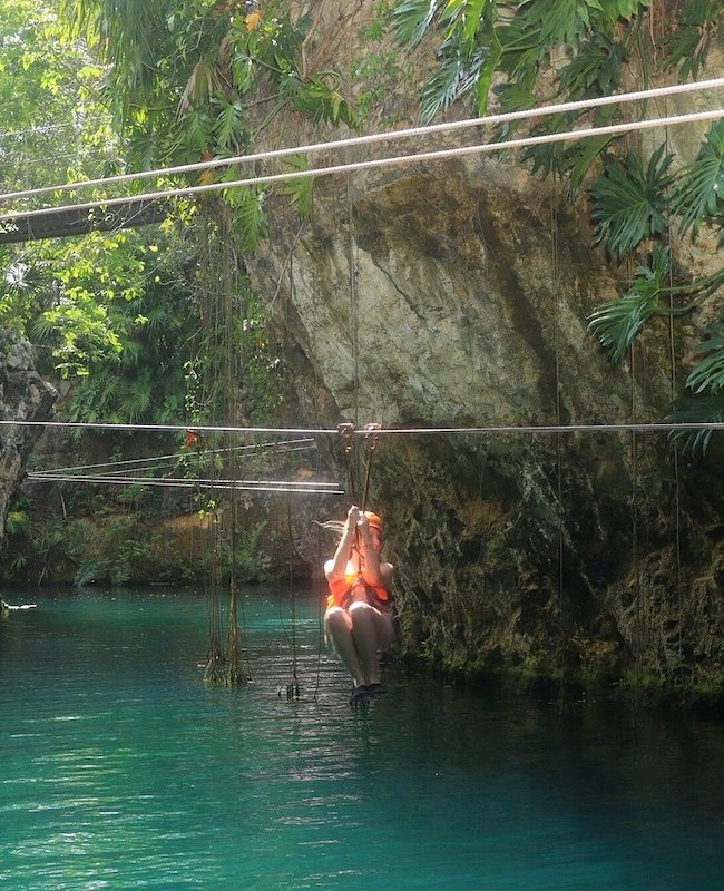 Woman with an orange helmet ziplining over water.