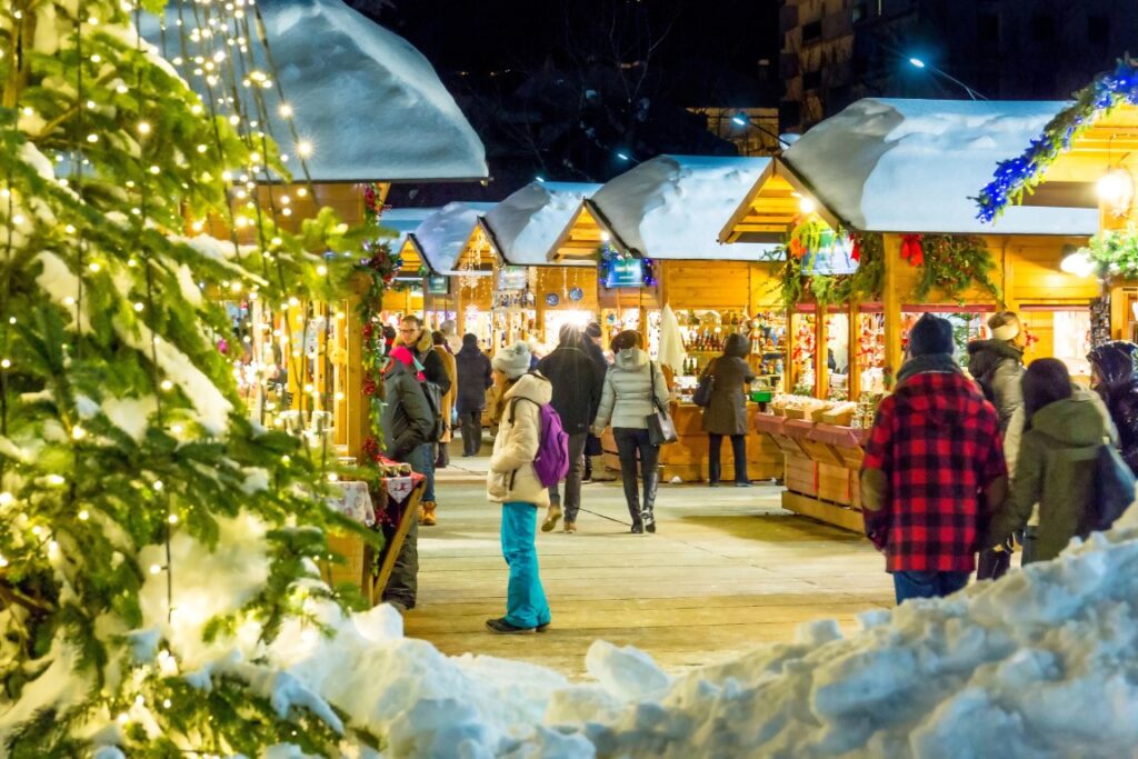 wooden stalls in a Christmas market with fake snow on their roofs