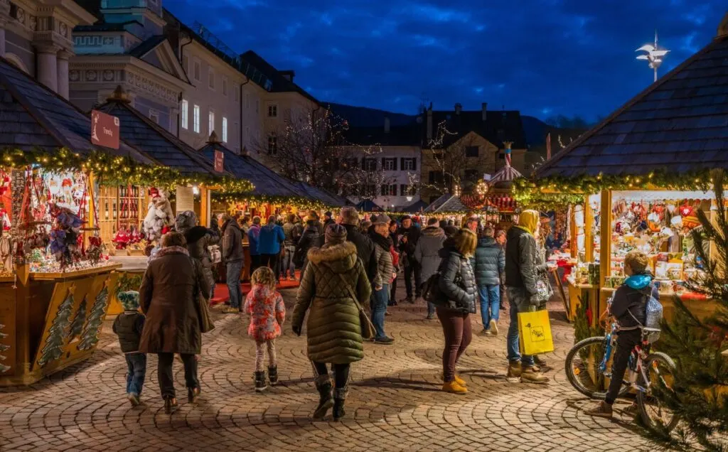 A nighttime image of a city's square with people walking around Christmas stalls