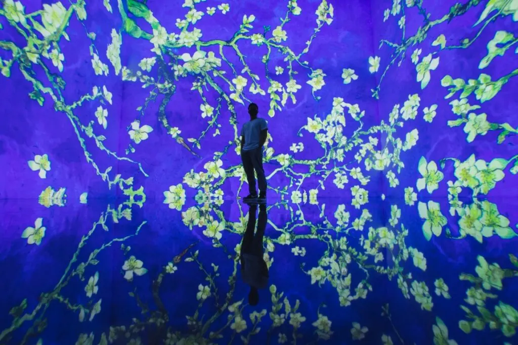 A man standing in the center of the image, completely surrounded by digital art of a blue background and yellow flowers