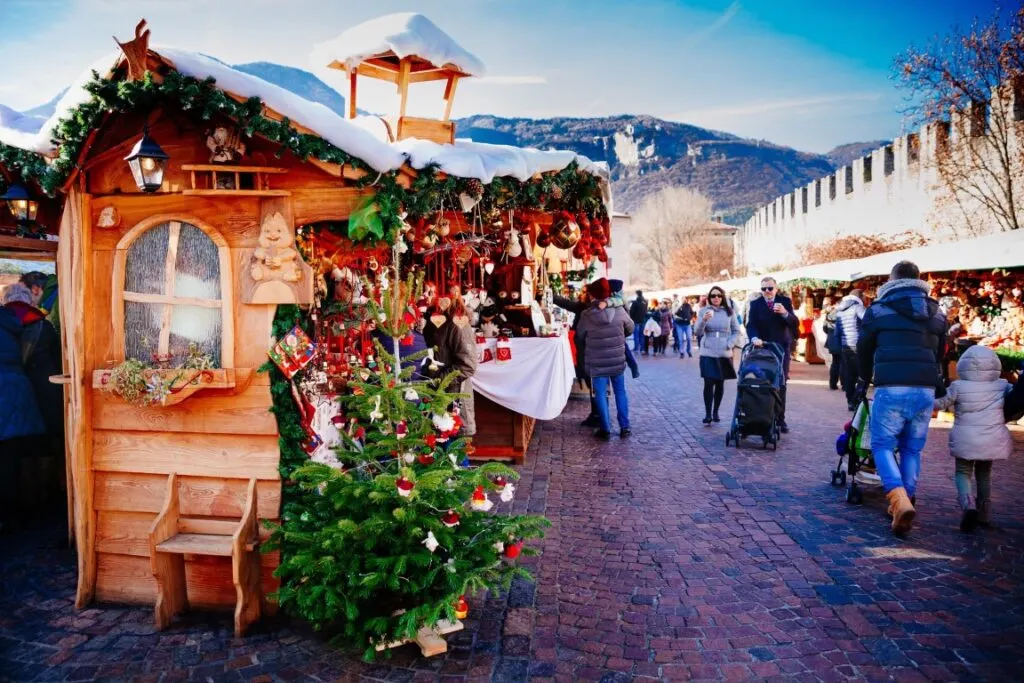 A wooden, heavily-decorated Christmas stall on the left of the image, and people walking on the right