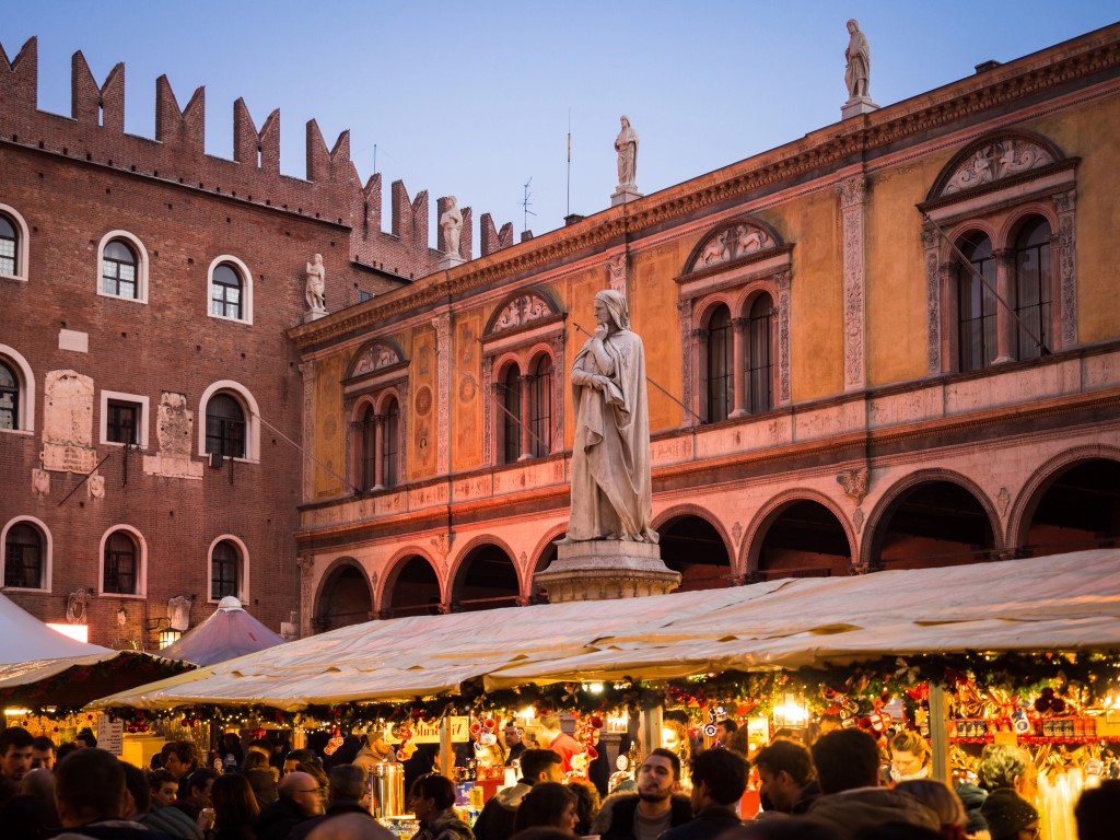 A Christmas market with a statue and a beautiful building in the background in Verona