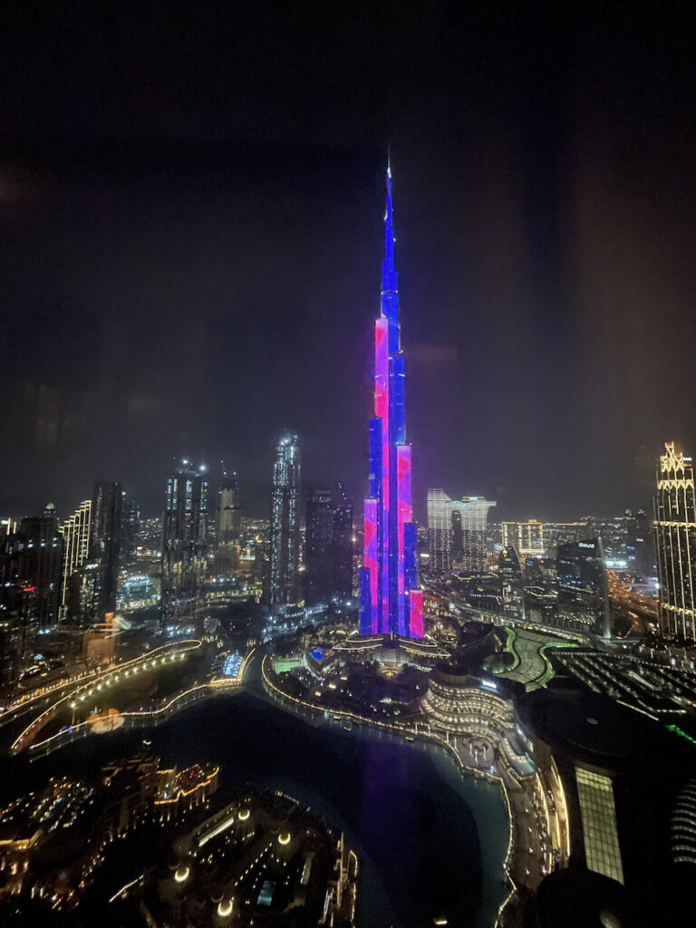 Burj Khalifa lit up in blue and pink lights, and the city of Dubai around it, the buildings lit up at night