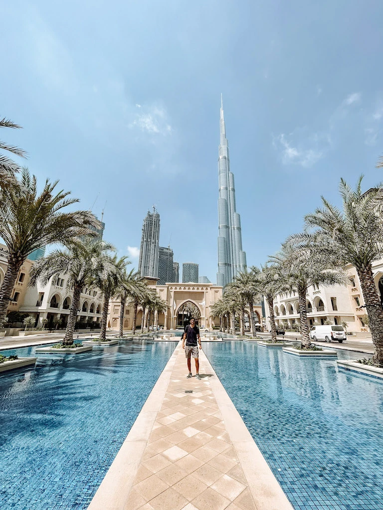 A man standing on a walkway in surrounded by water, with the Burj Khalifa and other skyscrapers in the background