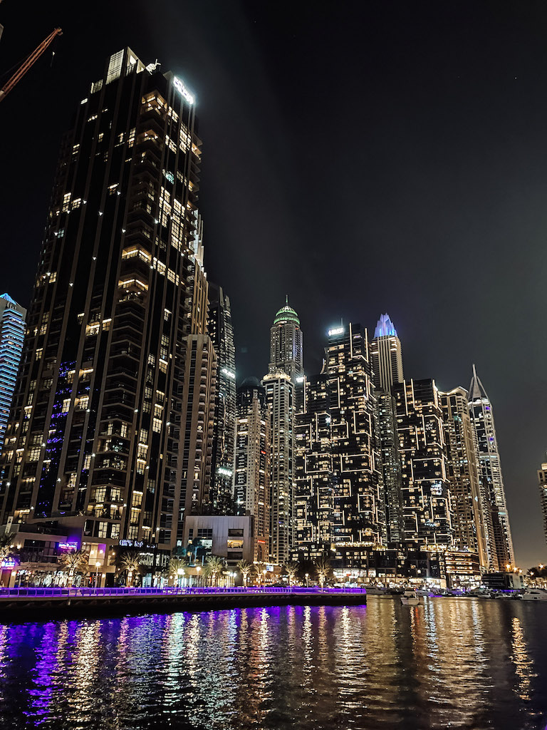 Skyscrapers in Dubai completely lit up at night, reflecting in the water at the forefront 