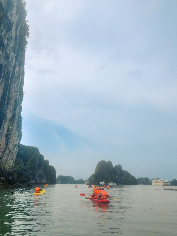 Multiple double kayaks with people wearing orange lifevests are paddling around Phang Nga bay.