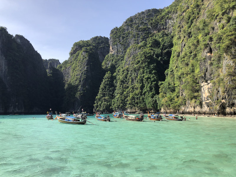 An image of Phi Phi islands with longtail boats on the turquoise sea waters, and karsts in the background