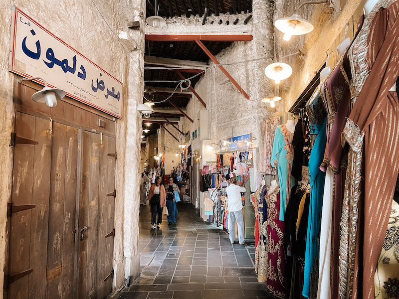 An alley lined by a wooden door on the left, and traditional dresses on the right in the Souq Waqif market