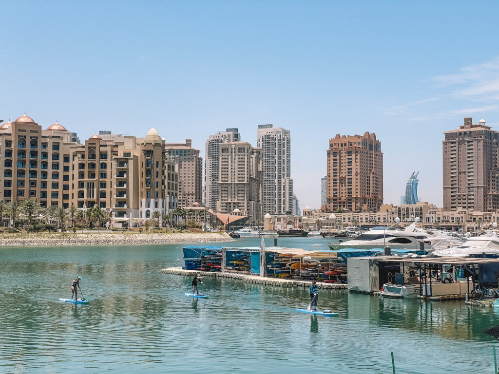 Three people paddleboarding next to a floating station with kayaks, and buildings in the background