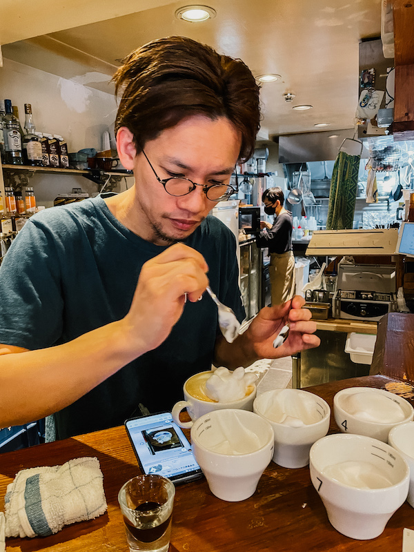 A Japanese man creating foam art on a coffee mug