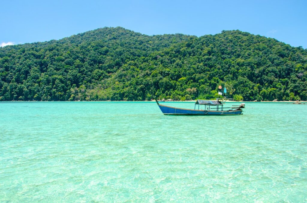 A longtail boat in crystal clear waters, and a mountain covered in vegetation in the background