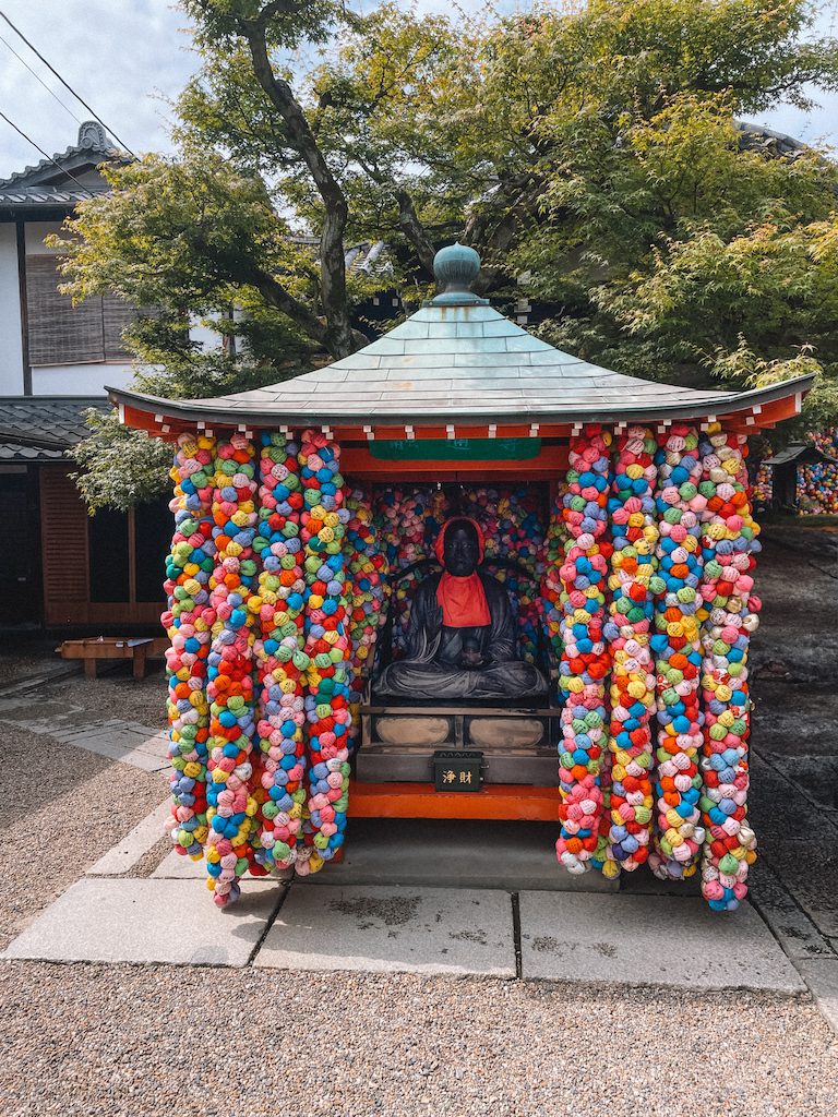 A small vermilion shrine surrounded by kukuri-zaru talismans and with the sculpture of a Shinto god inside