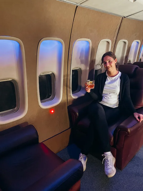 A woman sitting in an airplane chair holding a drink 