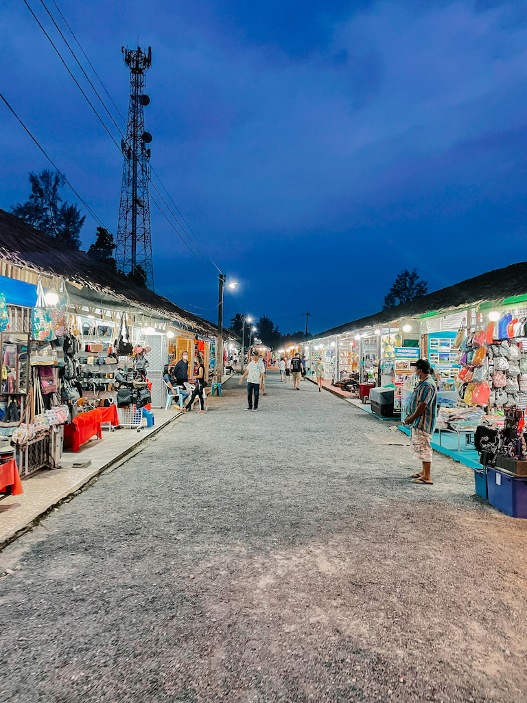 A gravel road lined by various stalls on both sides at night