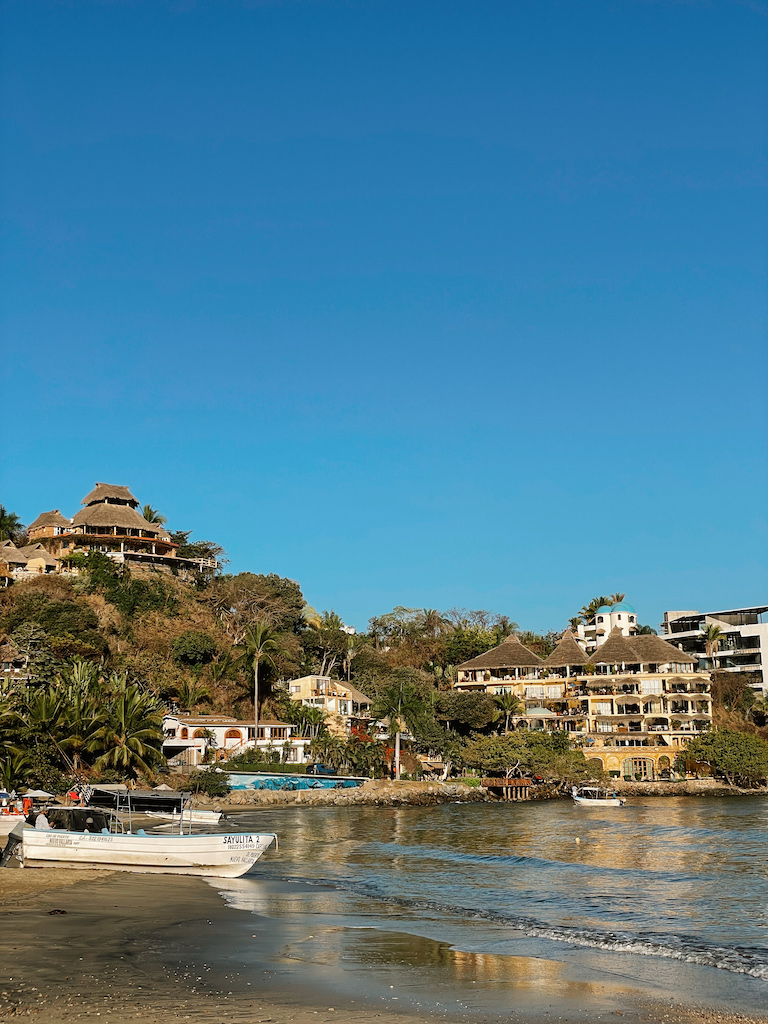 A beach with a white boat on the shore, and houses in the background