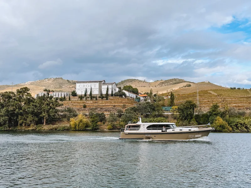 A boat cruising along a river, and a white building on the other side surrounded by hills and vegetation