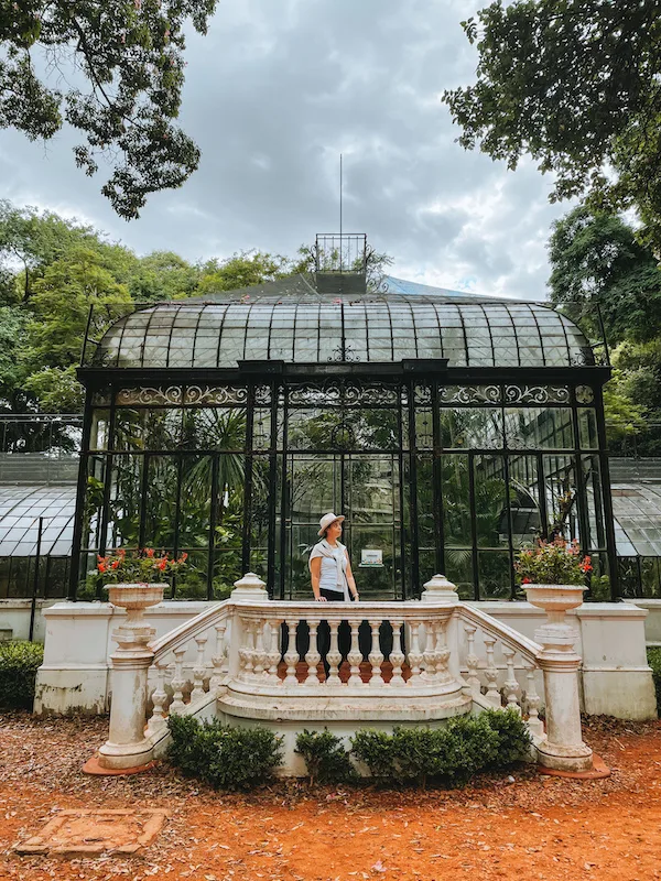 A woman  standing in a small ornate balcony outside a greenhouse