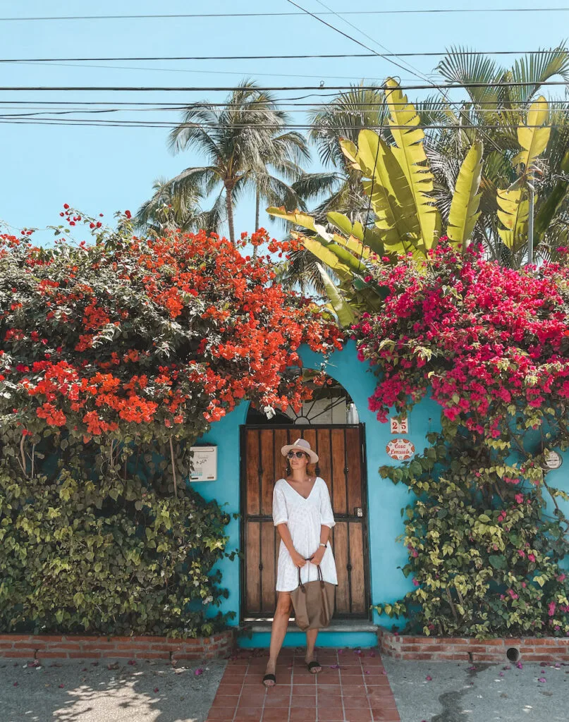 A woman in a white dress standing in front of a door full of colorful flowers