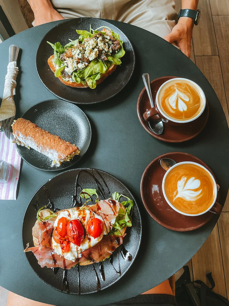 A round black table with two coffees, two breakfast toasts, and a cannoli