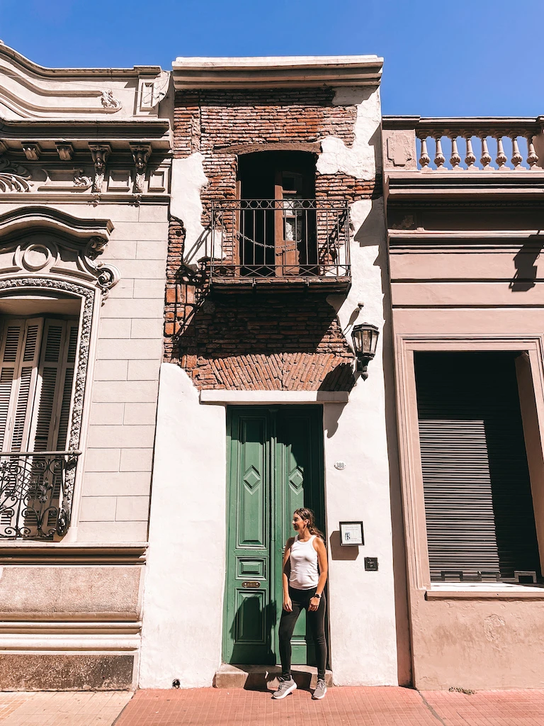 A woman standing in front of a green door in a very narrow, old-looking house