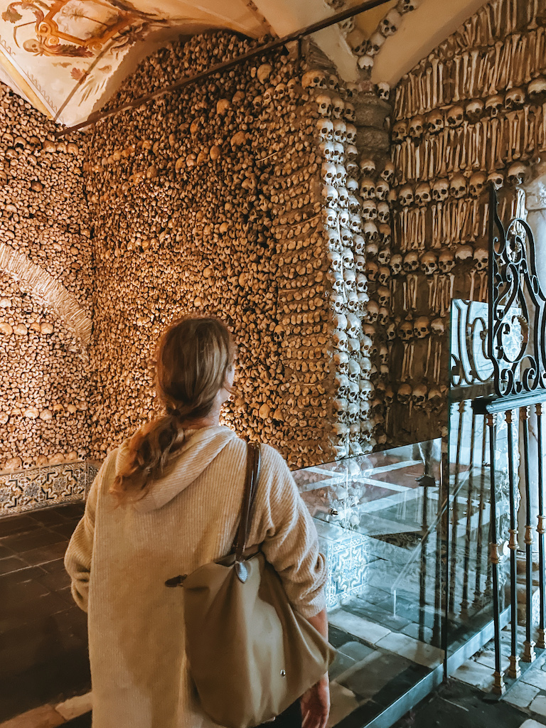 A woman inside a crypt that's fully decorated with bones and skulls