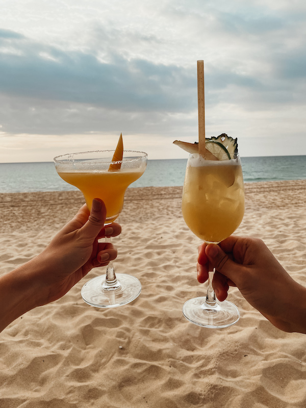 Two hands holding cocktail glasses at the beach 