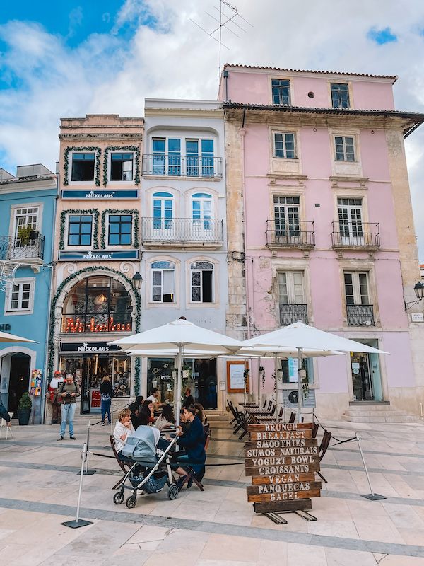 outdoor café tables with people sitting in one in front of tall, old-looking buildings 