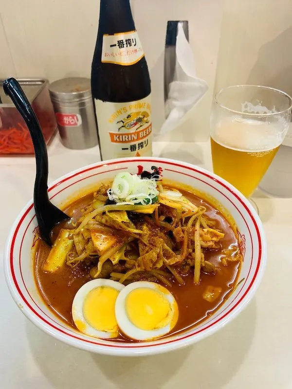 A bowl of ramen with a glass of beer and a bottle next to it 