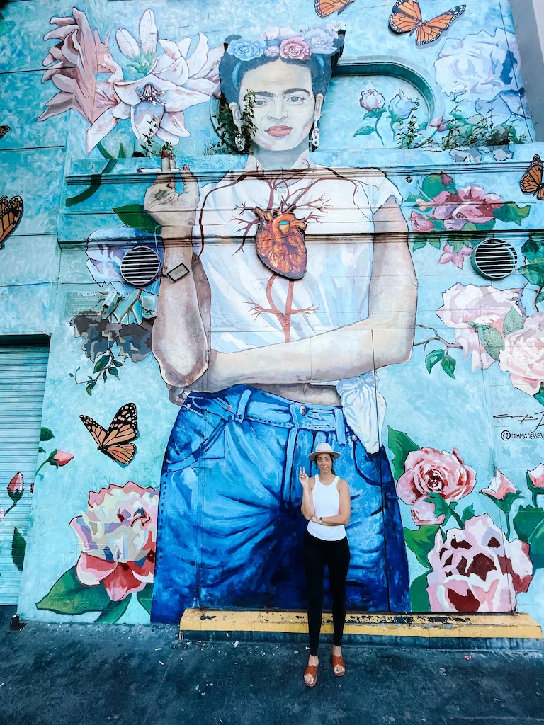 A painting of Frida Khalo and a woman posing in front of it 