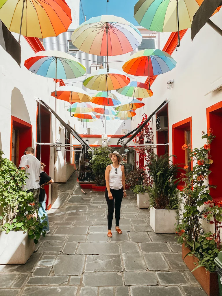 A woman standing under colorful umbrellas that hang above a courtyard