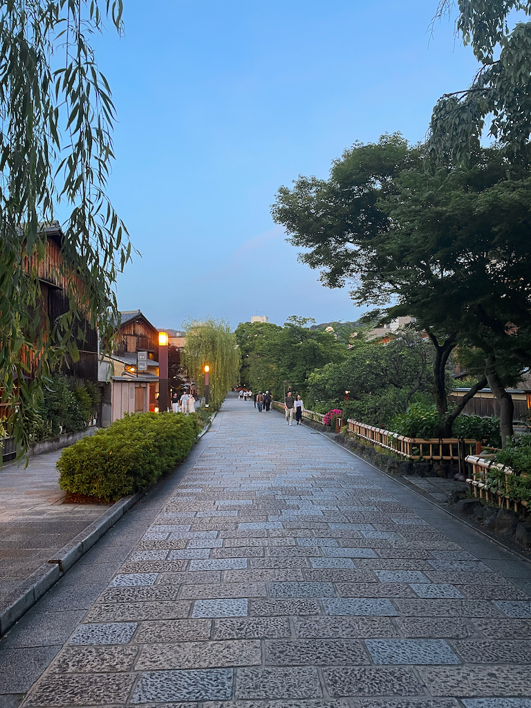 A street in Gion lined by trees and greenery in the evening.