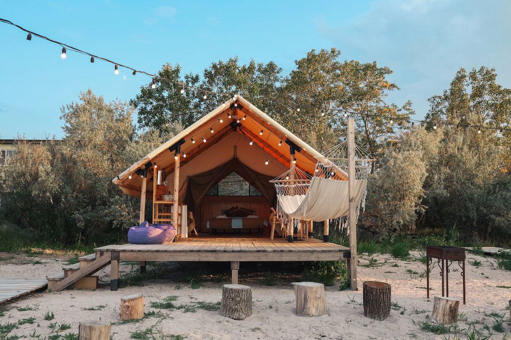 Image of a glamping tent in Portugal built on a wooden platform that works as a balcony. Here you find a white hammock and a purple blue bag.