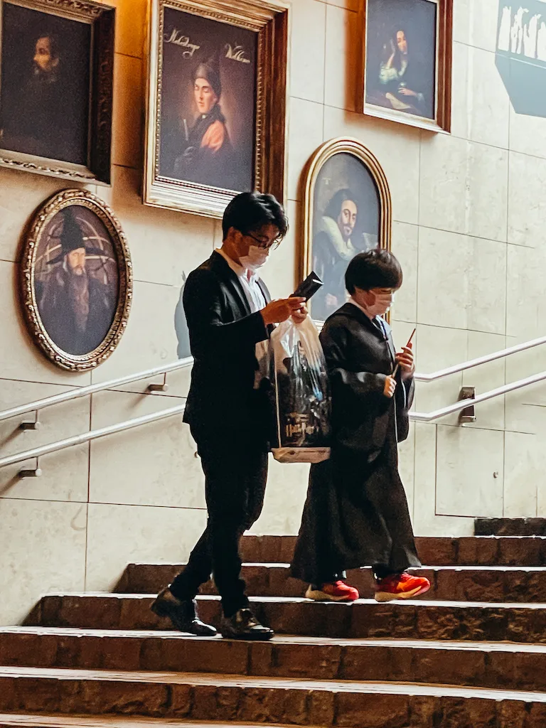 Two people standing on a staircase, photographing the walls that are covered in Harry Potter-themed paintings 