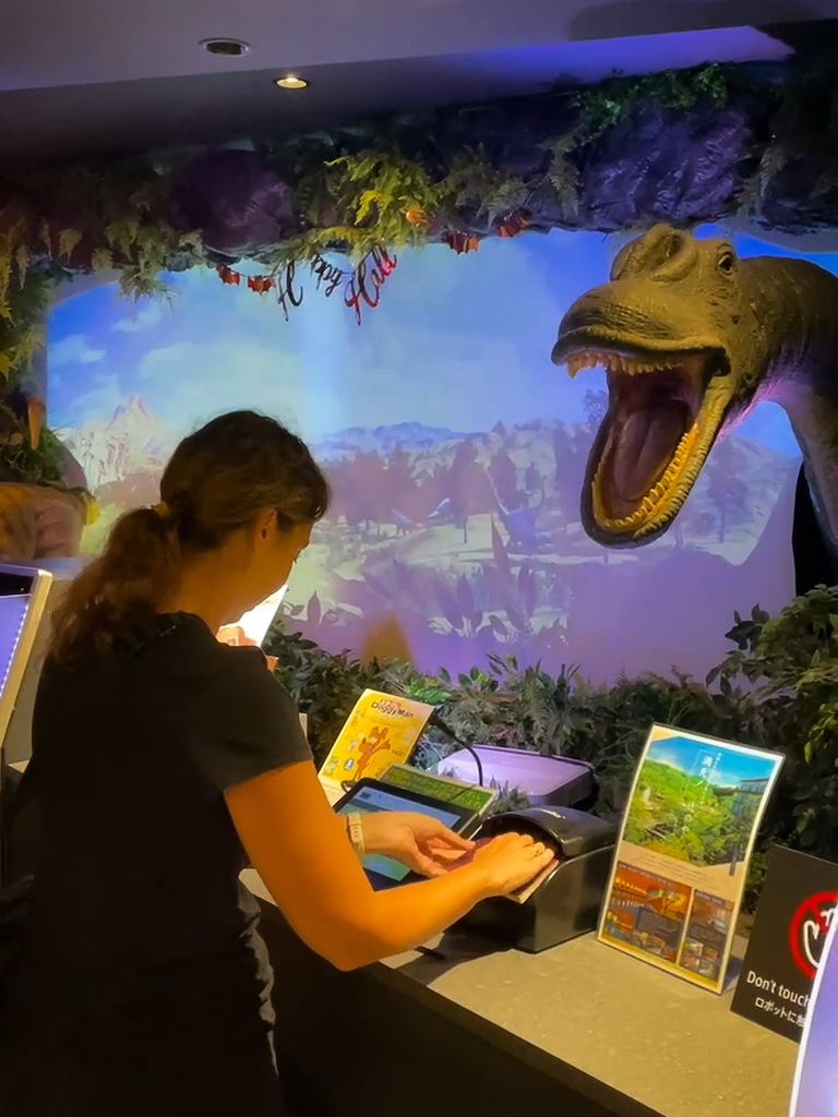 A woman checking in at a hotel with a dinosaur receptionist